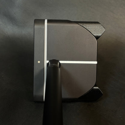 Close-up of a black golf club head and shaft, showing a matte finish with a thin white stripe detail, photographed on a dark textured surface.